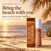 Beachy Bubbles Bath Co Coco Cabana Perfume Oil with its box beside a sunlit beach, highlighting its warm coconut-amber fragrance.